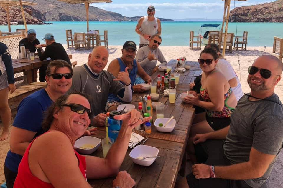 A group of travelers enjoying a meal and drinks at an outdoor table on a tropical island.